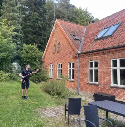 En af Domus' to ejere pudser vinduer med teleskopstang på en murstensvilla nær Jægerspris